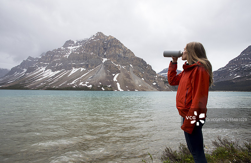年轻女人在冰川湖边喝瓶装水图片素材