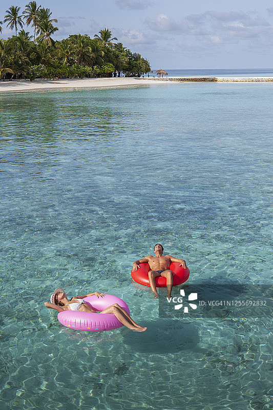 情侣躺在热带海水中充气泳圈上图片素材