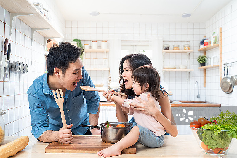 可爱的亚洲家庭在厨房里做饭，面带微笑的母亲、父亲和孩子们站在烹饪台旁，食材放在桌子上图片素材