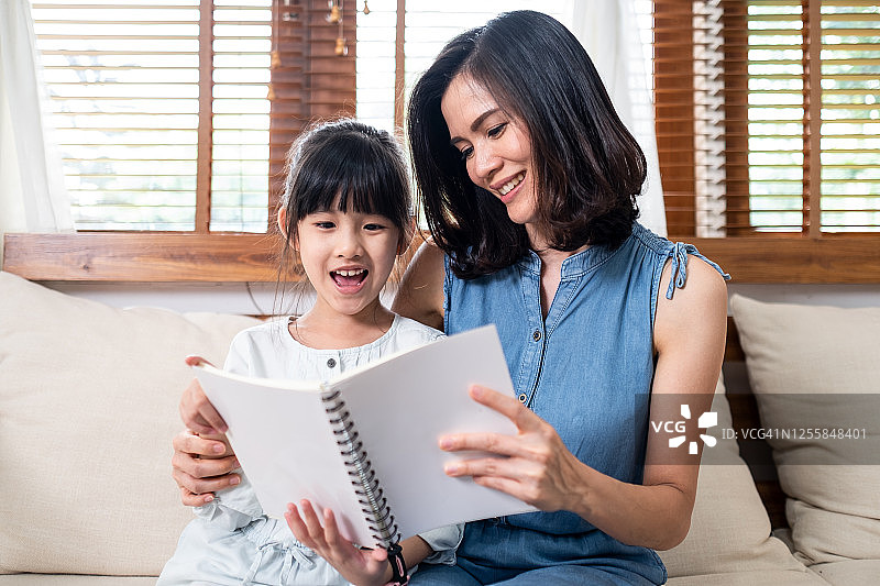 亚洲母亲和女儿在客厅一起读书图片素材