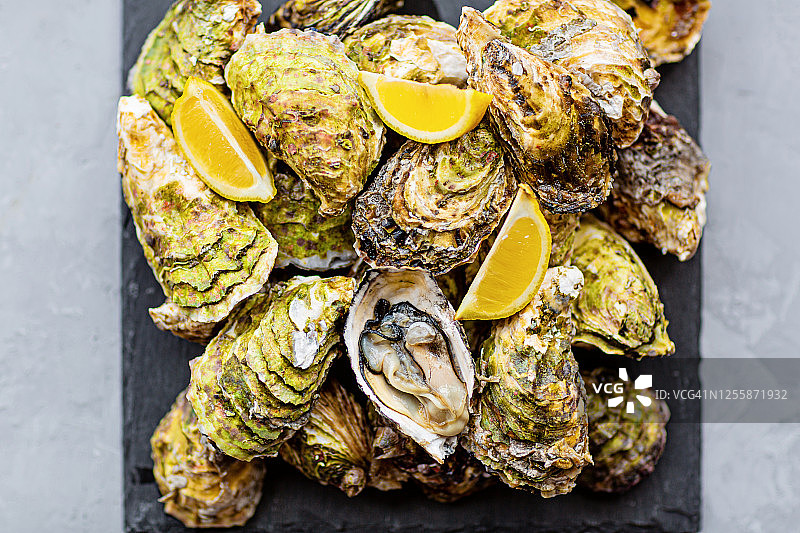 黑盘中配柠檬和冰块的新鲜生蚝特写，健康海鲜，美食，平面，顶视图，模型，俯视，带复制空间的模板，在线订购和食品配送图片素材