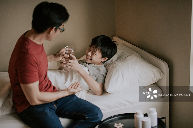 中国亚洲男孩生病后在床上从父亲那里得到药和药丸图片素材