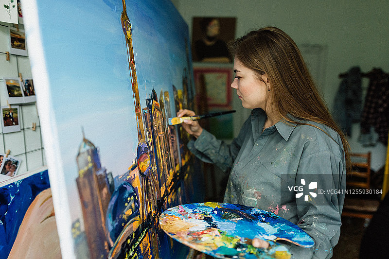 年轻白人女子在家中艺术工作室绘画城市景观图片素材