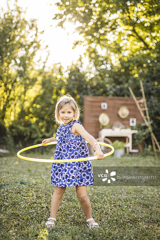 穿着连衣裙的快乐小女孩在户外玩呼啦圈图片素材