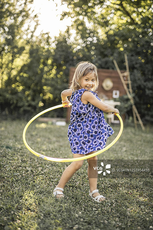 穿着连衣裙的快乐小女孩在户外玩呼啦圈图片素材