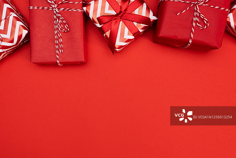 红色背景上的圣诞礼物。简约、经典的红色和白色包装礼品盒，带有丝带蝴蝶结和节日装饰。水平底部边框。图片素材
