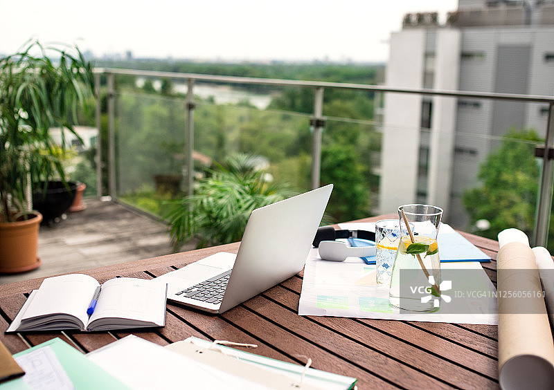 办公桌上的笔记本电脑和蓝图，城市阳台上的户外家庭办公室图片素材