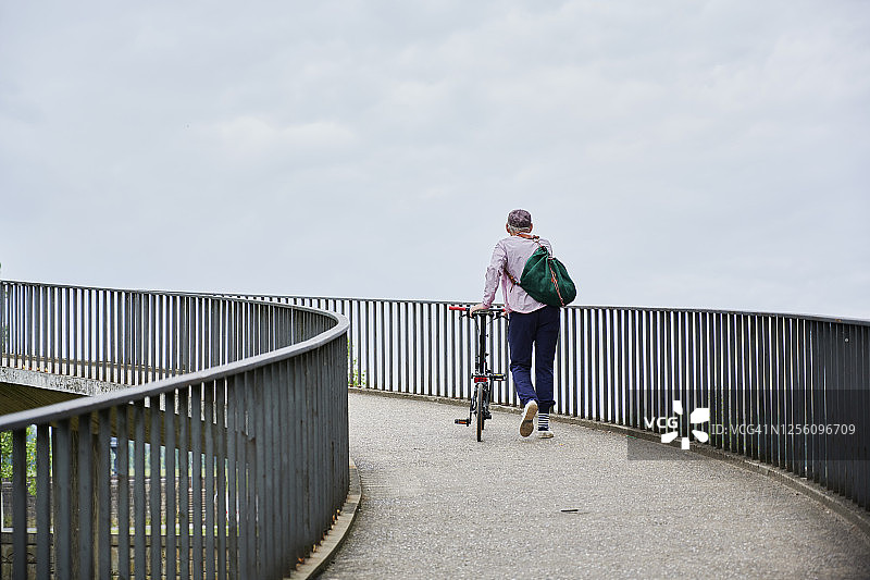 年长的男人在桥上推着他的折叠自行车图片素材