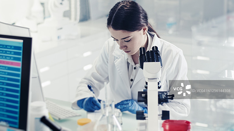 女医生在研究中做笔记，在基因研究实验室使用显微镜图片素材