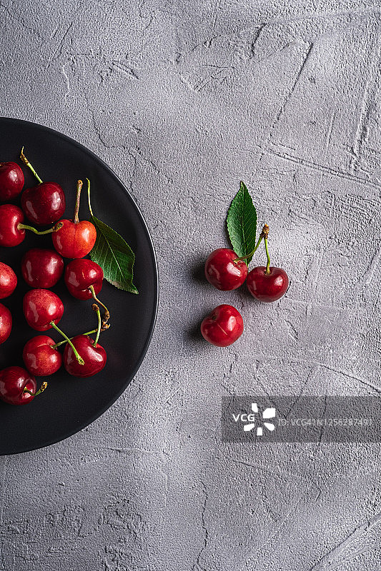 黑色盘子中带有绿叶的新鲜成熟樱桃，灰色石材背景上的夏季维生素浆果，顶视图图片素材