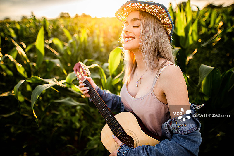 田野里弹吉他的一位美丽的年轻女人图片素材