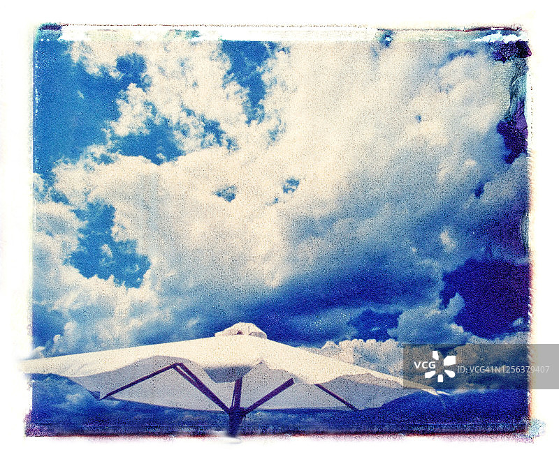 被风吹拂的白色市场遮阳伞和引人注目的天空与白色蓬松的云彩 - 宝丽来转移照片 - 系列的一部分图片素材