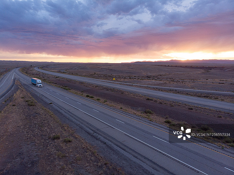 在黄昏或黎明时荒凉沙漠中四车道高速公路上行驶的长途货运半挂卡车和拖车图片素材