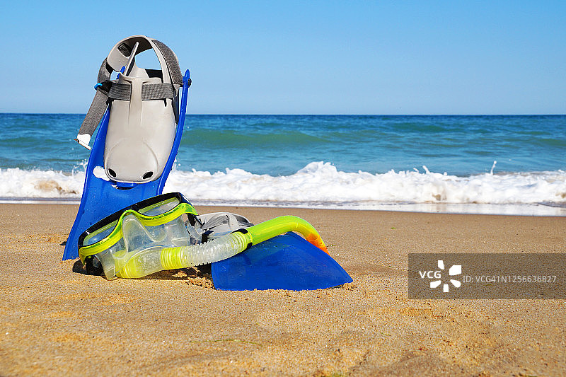 沙滩上的游泳脚蹼和面罩，背景为大海和晴朗的天空，留白区域图片素材
