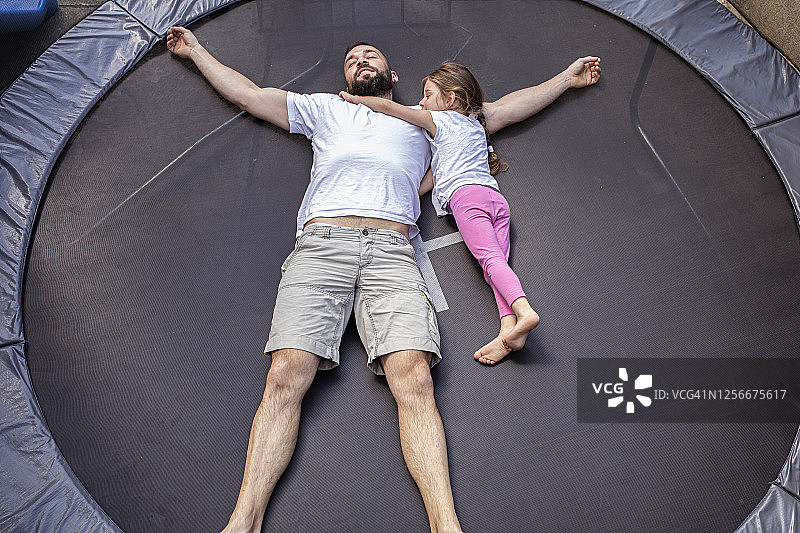 父亲和小女儿躺在蹦床上图片素材