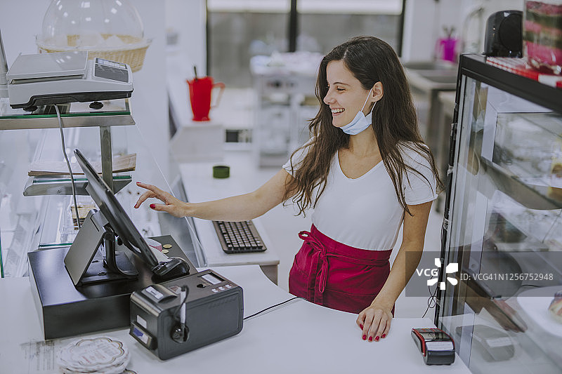 友好的收银员面带微笑，在糖果店的收银台后图片素材