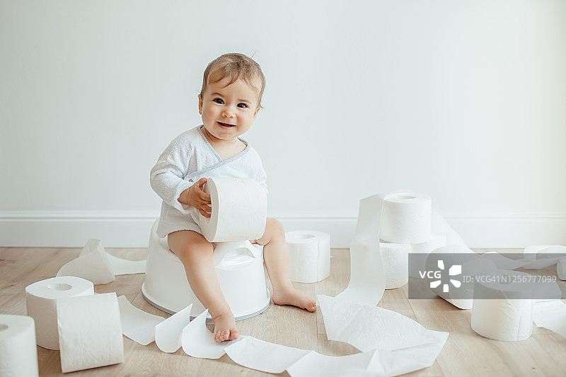 可爱的女宝宝坐在白色便盆上玩卫生纸图片素材