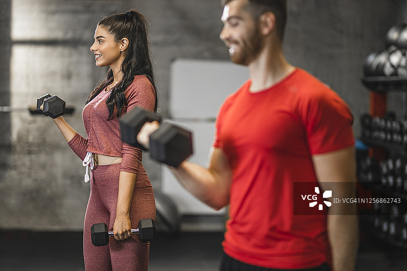在健身房里用哑铃锻炼并微笑的美丽年轻运动员图片素材