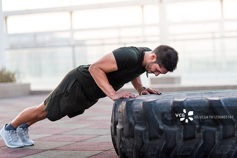 男人在户外锻炼时在拖拉机轮胎上做俯卧撑图片素材