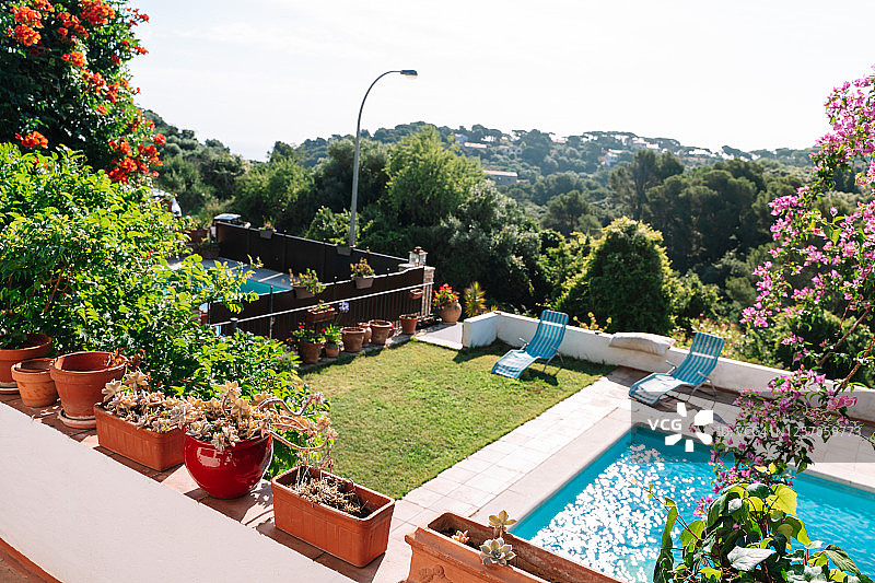 阳台鸟瞰：游泳池、日光浴床，周围环绕着树木和有建筑的山丘图片素材