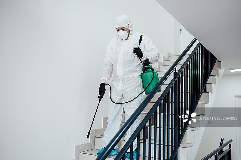 室内表面消毒清洁。建筑物内部清洁与消毒，预防新型冠状病毒。专业消毒团队进行消毒工作。预防和控制疫情感染。防护服和口罩。图片素材