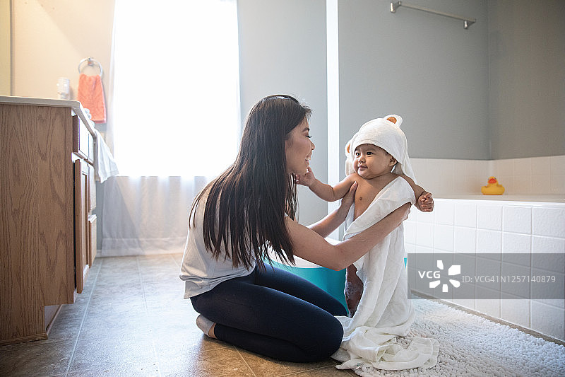 宝宝在浴室泡泡浴后，妈妈用毛巾包裹着他，宝宝触摸着妈妈的脸图片素材
