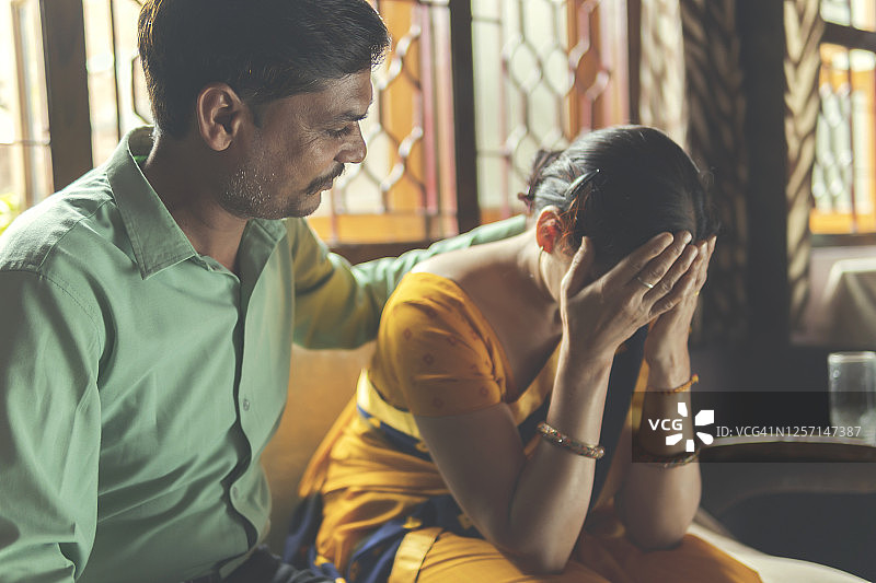 女人抱着头，感到沮丧、头痛，她的丈夫正在安慰她图片素材