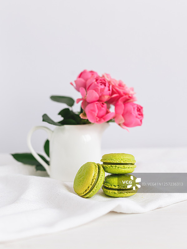 三个美味的法式马卡龙和一个装满美丽玫瑰的罐子，白色背景，有文字空间图片素材
