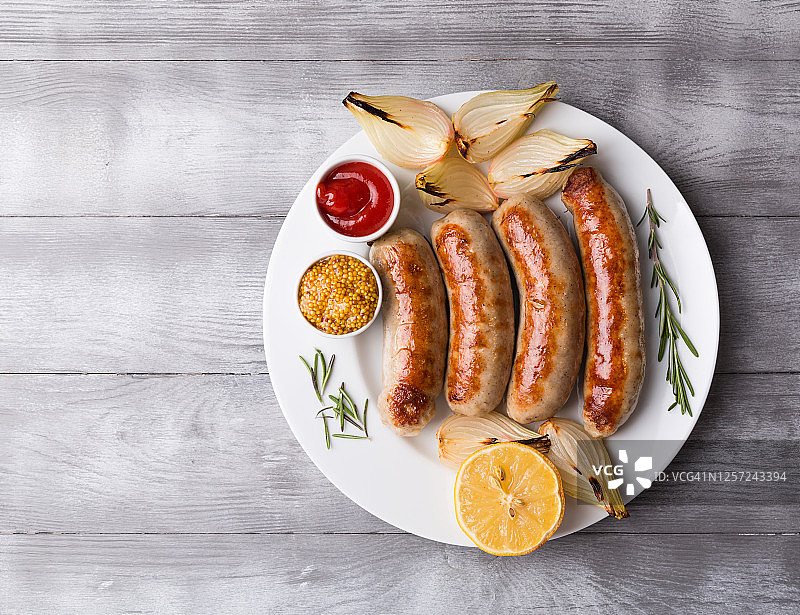 自制香辣烤香肠配烤蔬菜和香料，浅色木纹背景。特写，留白图片素材