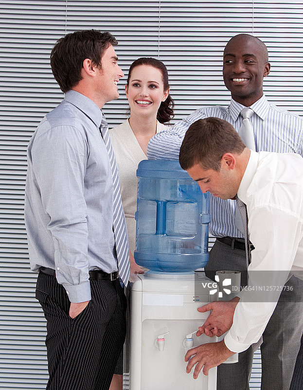 在饮水机旁互动的微笑的商人们图片素材