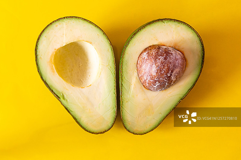 黄色背景上的两片鳄梨，一片带核图片素材