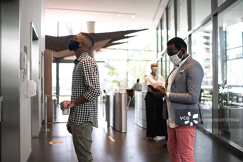 同事在办公室大堂戴着口罩等候电梯图片素材