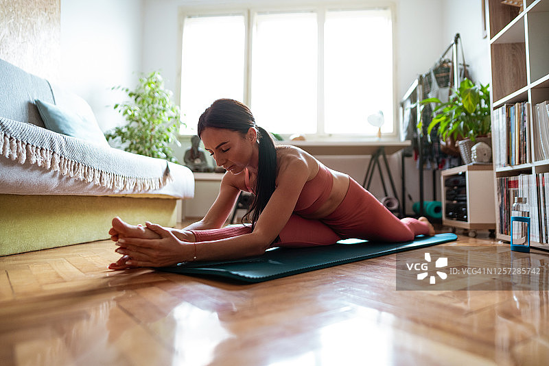 在家中瑜伽垫上做劈叉的女人图片素材