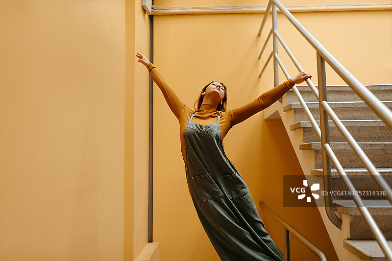 穿着连身裤站在橙色墙前的年轻女人图片素材