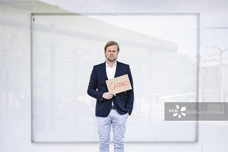 站在白墙前拿着“关闭”标志的商人肖像图片素材