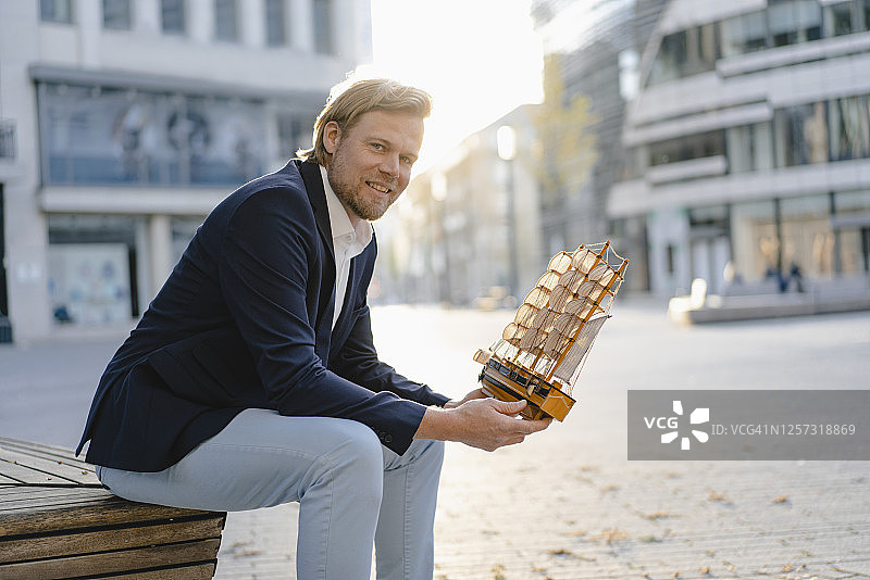 坐在城市长椅上拿着模型船的商人图片素材