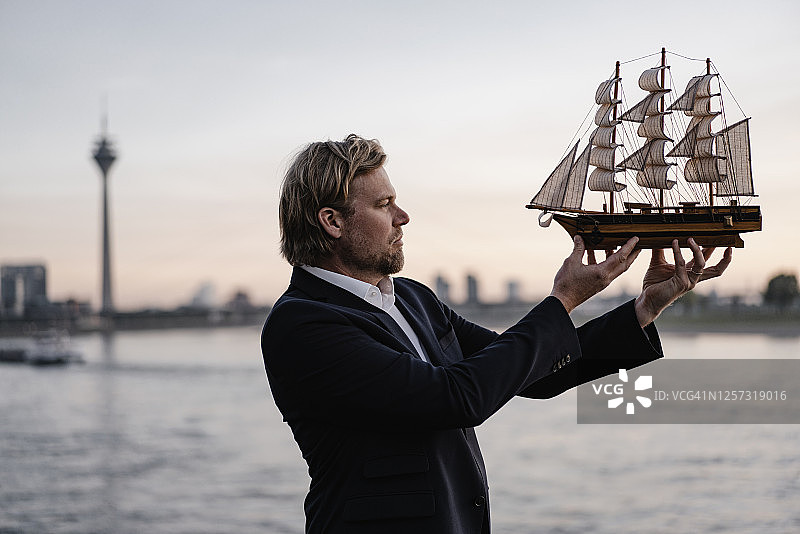 商人黄昏时在河边手持模型船图片素材