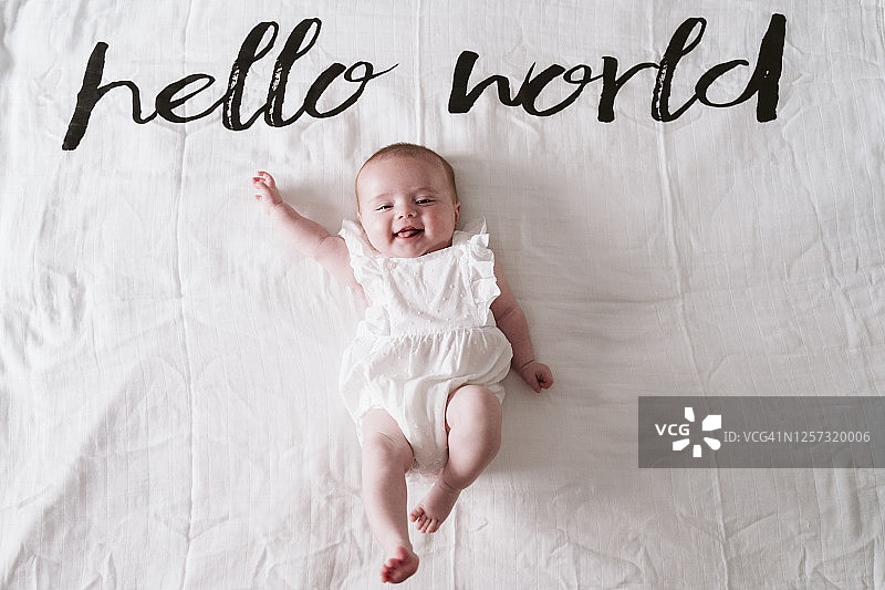 快乐的可爱女婴躺在Hello World文字下的毯子上图片素材