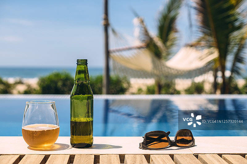 夏季户外游泳池边的太阳镜和打开的啤酒图片素材