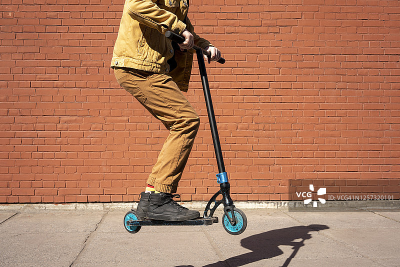 男孩在人行道上用滑板车表演特技，背景是砖墙图片素材