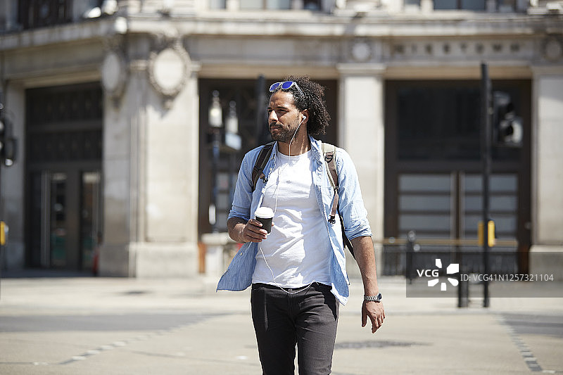 英国伦敦，戴着耳机听音乐过马路的年轻男子肖像图片素材