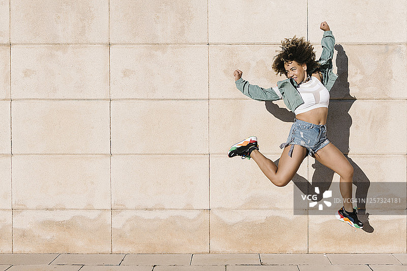 在阳光明媚的日子里靠墙跳跃的兴奋年轻女子图片素材