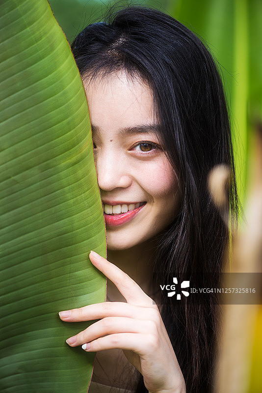 树叶后面的中国年轻女人自然肖像图片素材