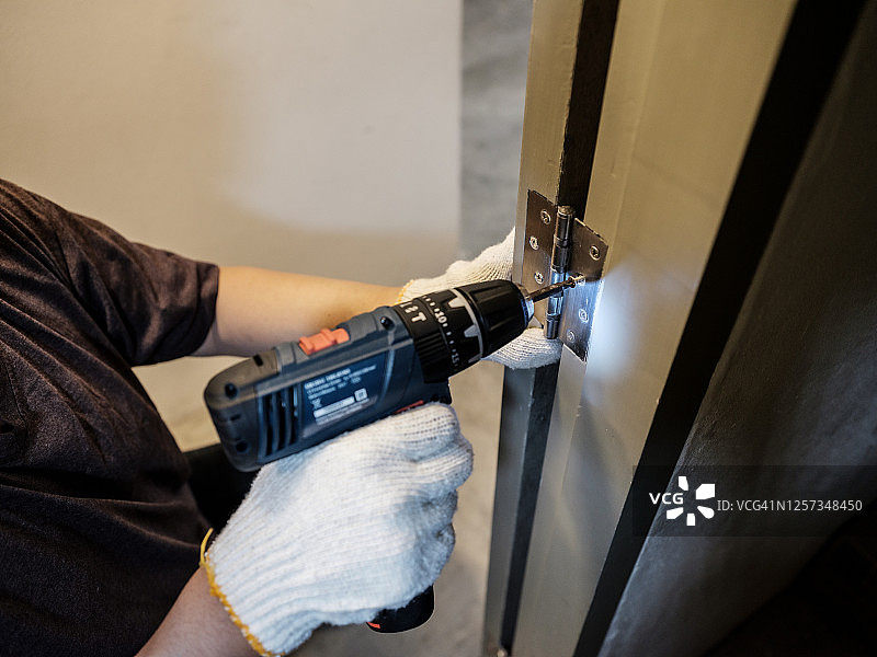 家居装修：用电动螺丝刀固定门上的蝶形铰链图片素材