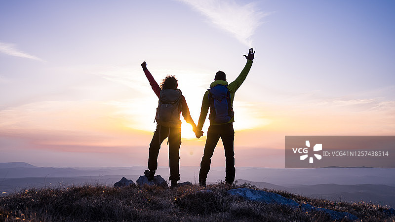 在山顶上抬起手臂看太阳的情侣图片素材