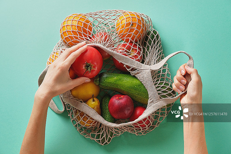 绿色背景下女人环保购物袋装新鲜蔬果图片素材