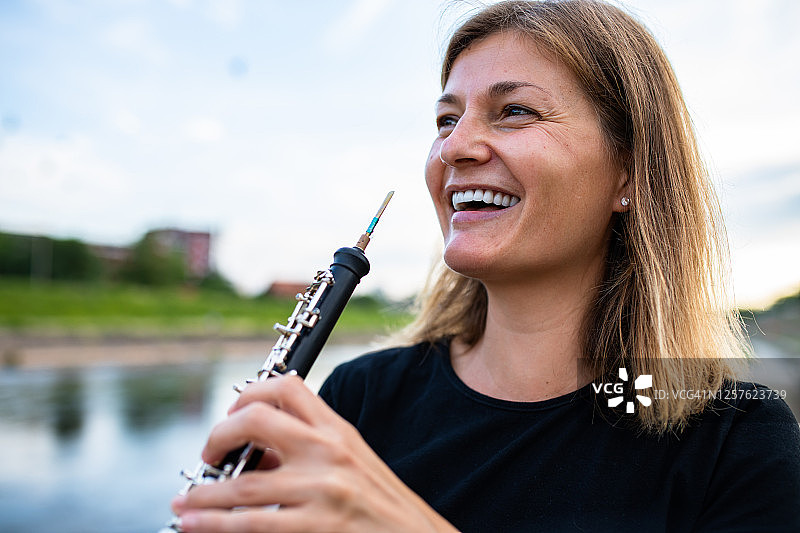 一位金发女子在河边拿着双簧管对着嘴巴微笑图片素材