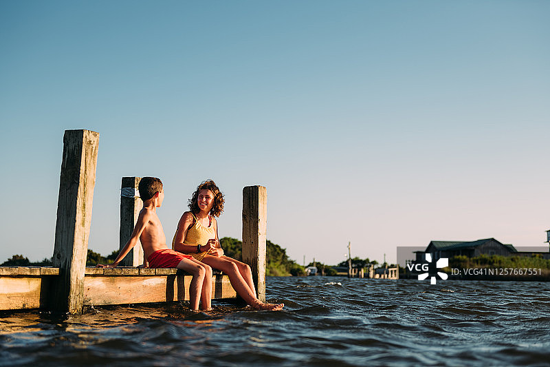 兄妹在码头上把脚浸在水里图片素材