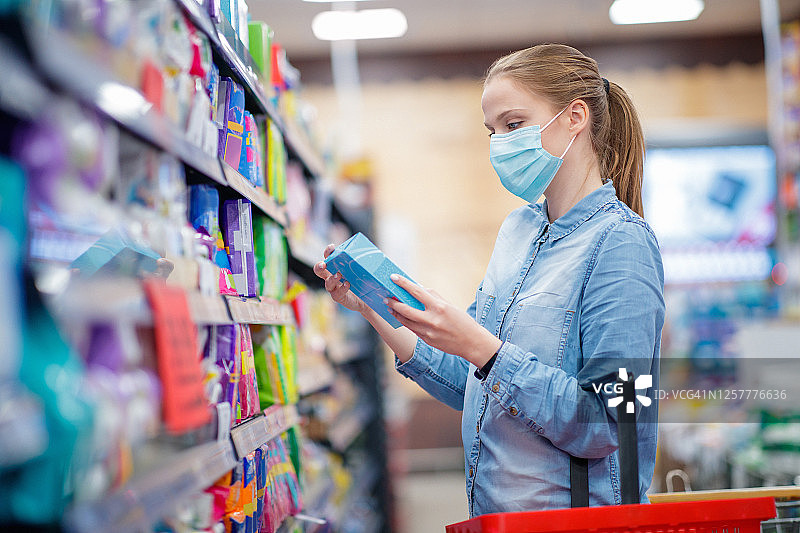 戴防护口罩的年轻女人在超市里拿着一盒卫生巾图片素材