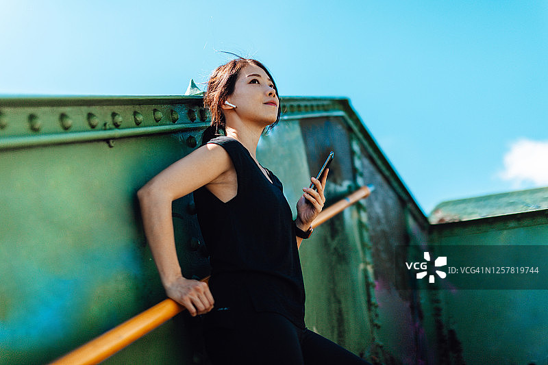 在艺术区城市中心，手持智能手机仰望天空的年轻女跑步者图片素材